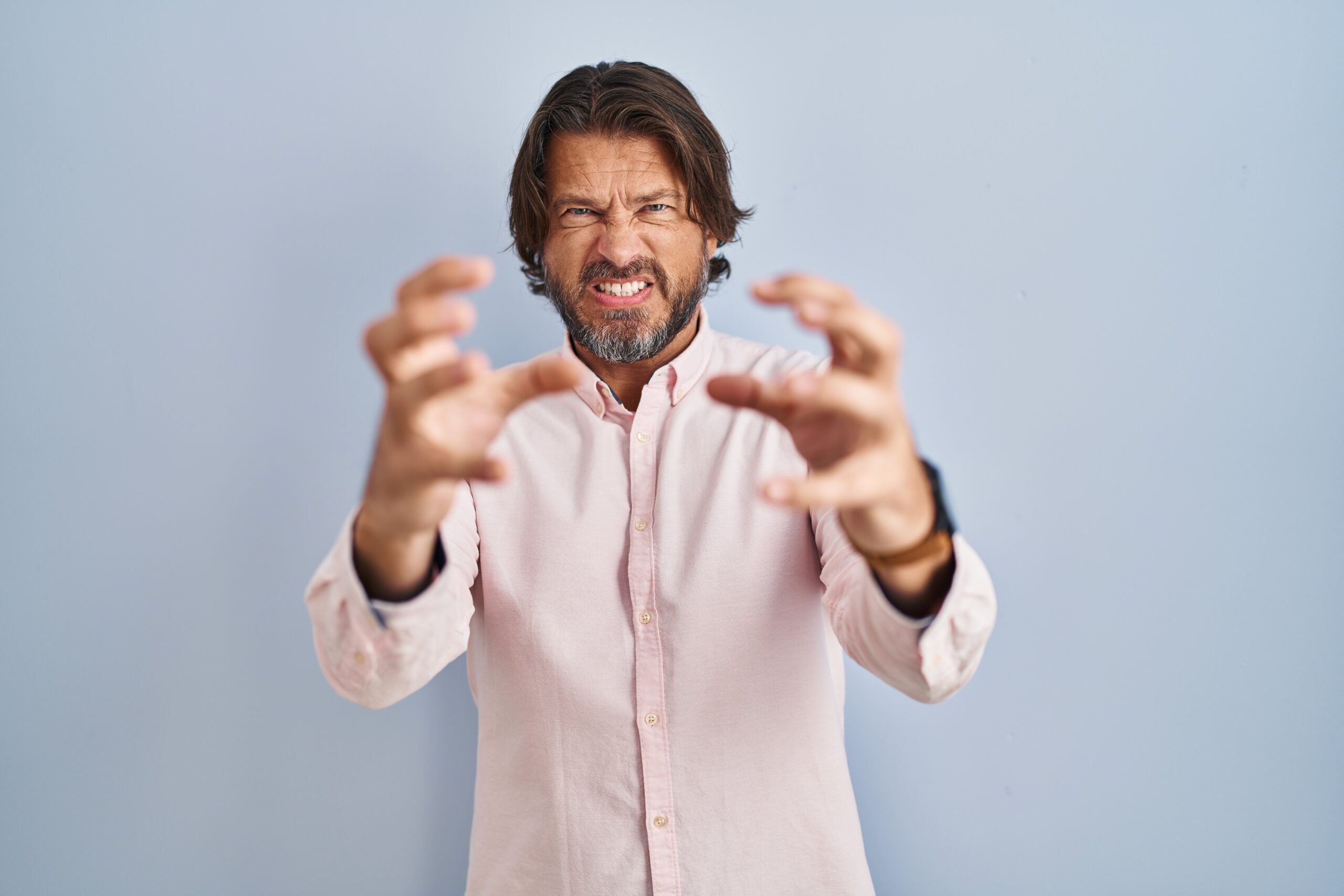 Handsome middle age man wearing elegant shirt background shouting frustrated with rage, hands trying to strangle, yelling mad